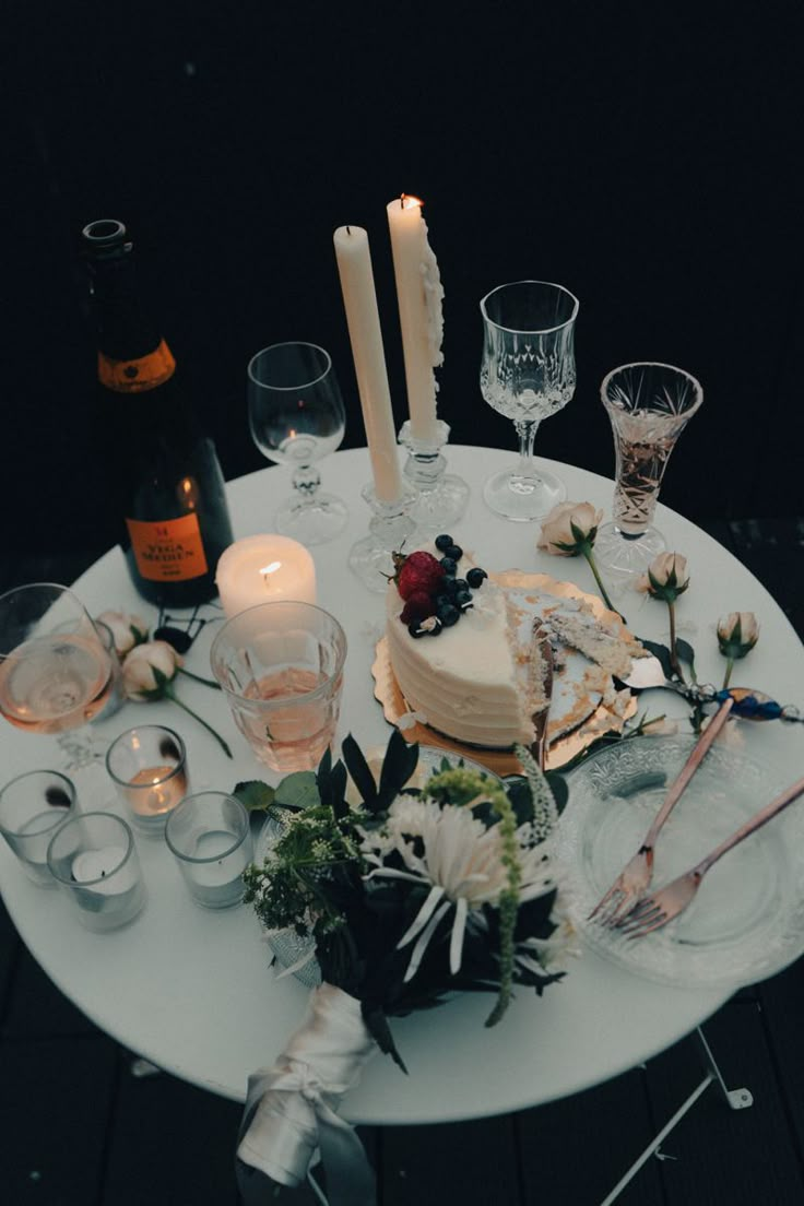 the table is set with candles, wine glasses and cake for an elegant dinner party