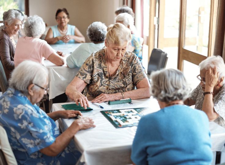 an elderly woman playing checkers at a table with other older women in the background