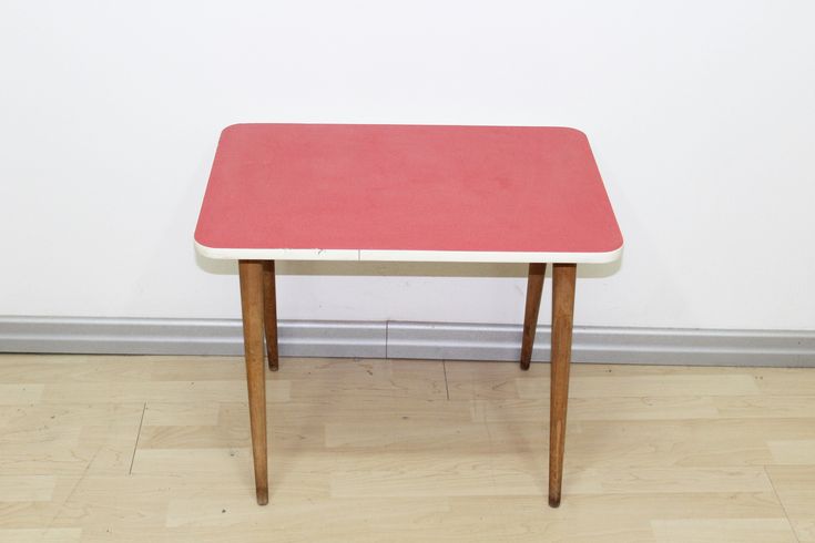 a small red table sitting on top of a hard wood floor next to a white wall