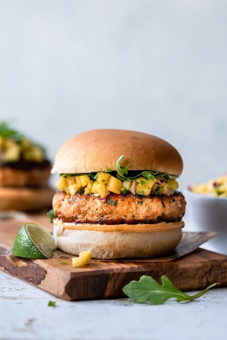 a chicken burger sitting on top of a wooden cutting board next to a bowl of salsa