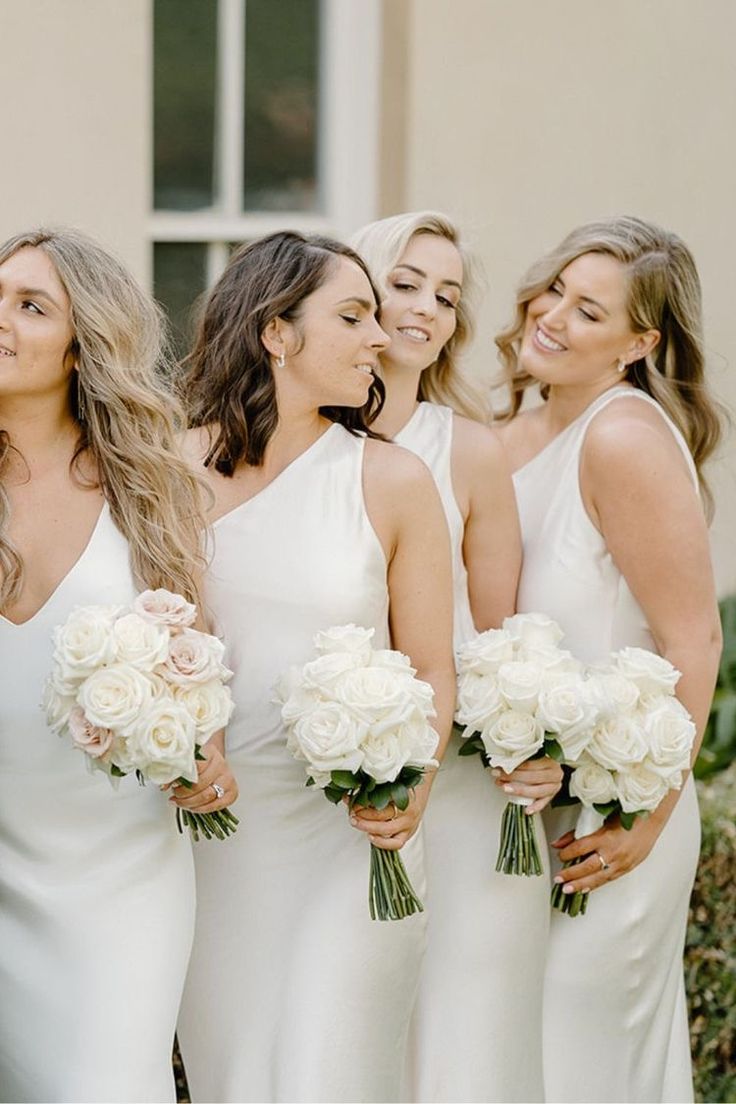 a group of women standing next to each other in white dresses holding bouquets and smiling