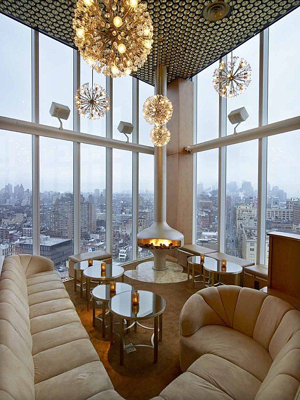 a living room filled with lots of furniture and large windows next to tall buildings in the background