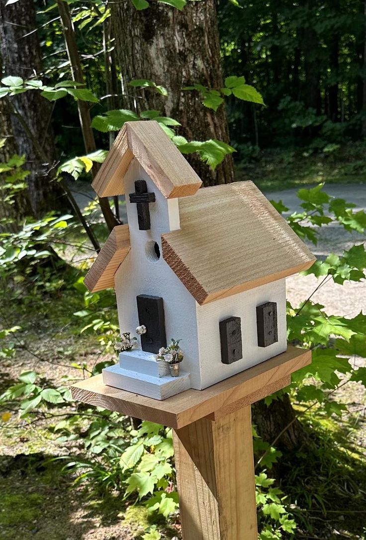 a small white house sitting on top of a wooden post in front of some trees