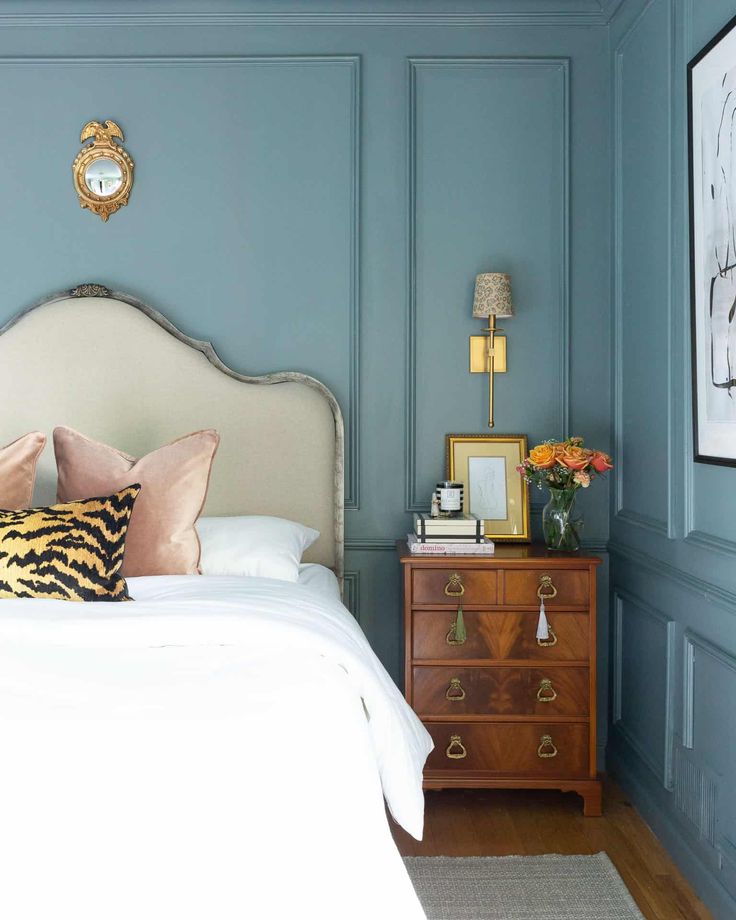 a bedroom with blue walls and white bedding, gold clock above the headboard