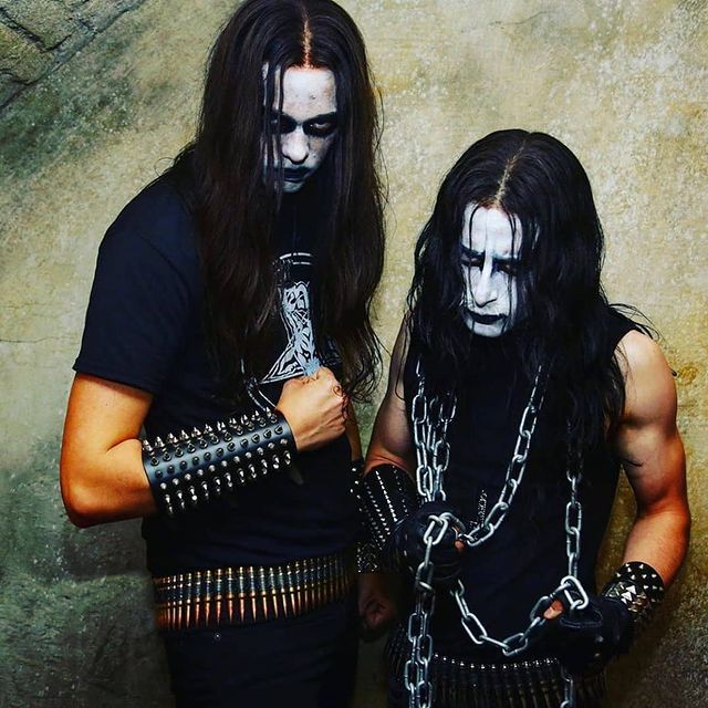 two men dressed in black with chains and makeup on their faces, standing next to each other