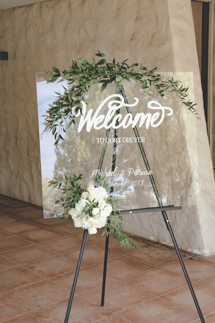 a welcome sign with flowers on it in front of a stone wall and tile floor