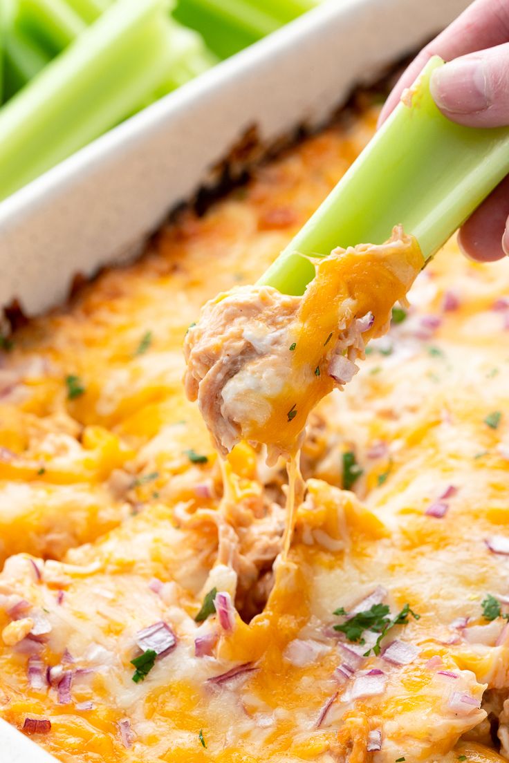 a hand holding a green toothpick over a casserole dish filled with chicken and cheese