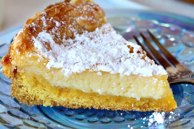 a piece of pie with powdered sugar on top sits on a blue glass plate