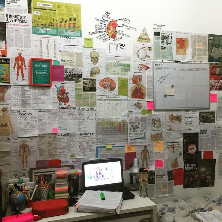 a desk with a laptop computer sitting on top of it next to a wall covered in papers