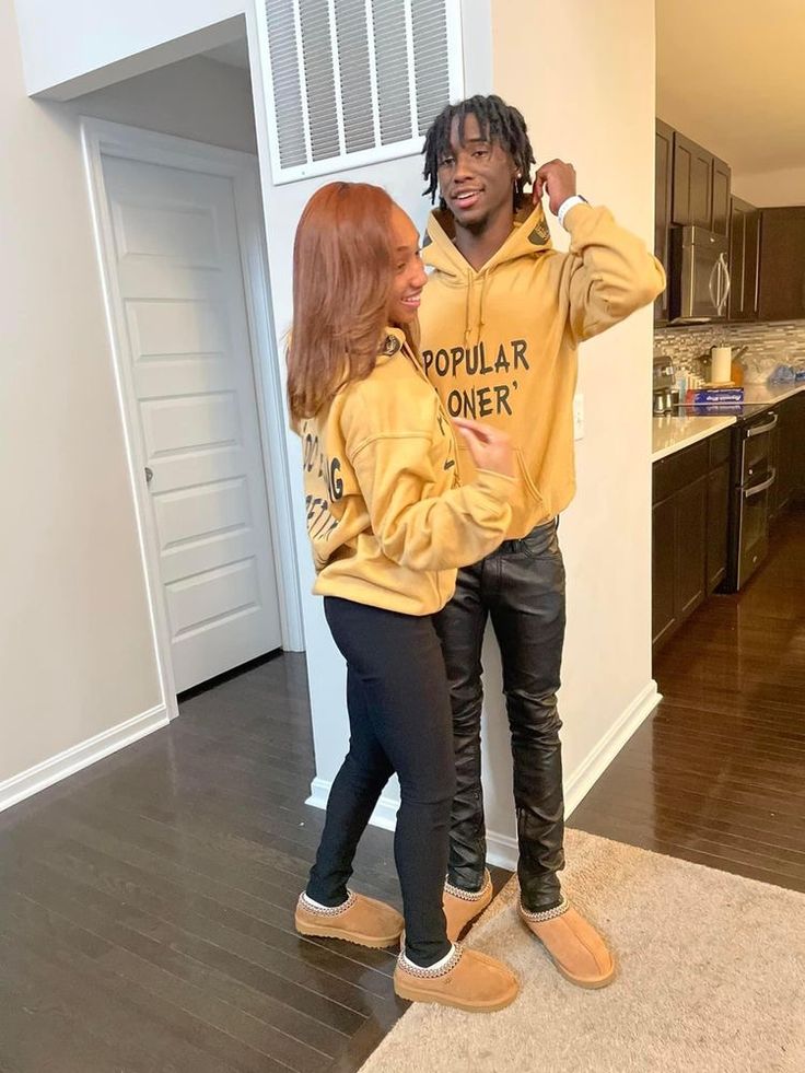 two people standing in the middle of a living room wearing yellow sweatshirts and black pants