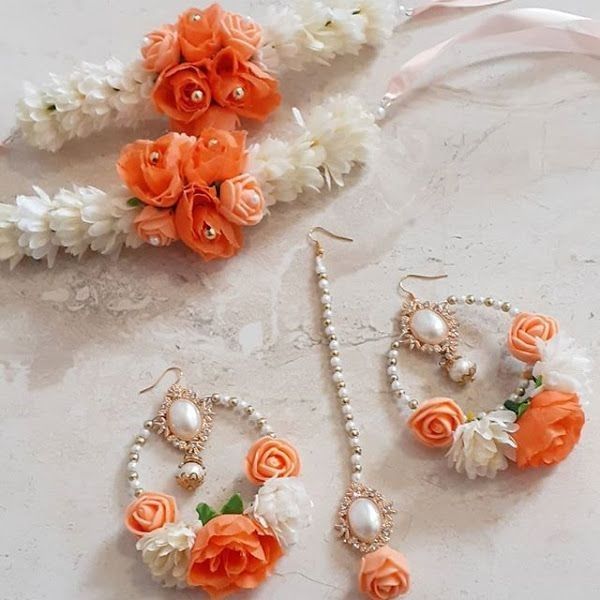 three pieces of jewelry on a table with flowers and pearls around it, including an orange flower