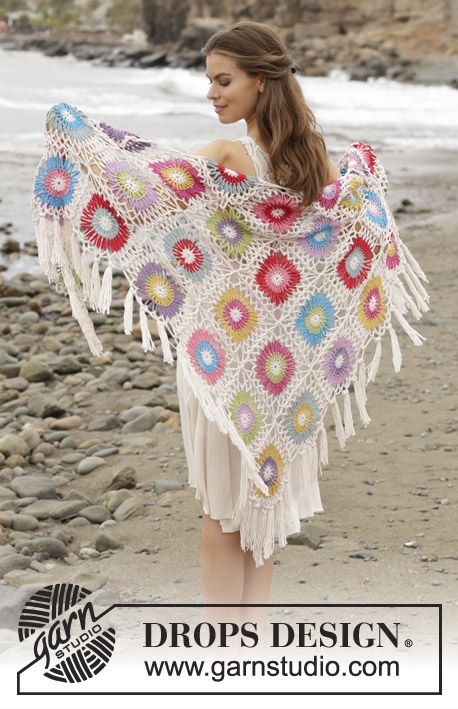 a woman is standing on the beach holding a crocheted shawl