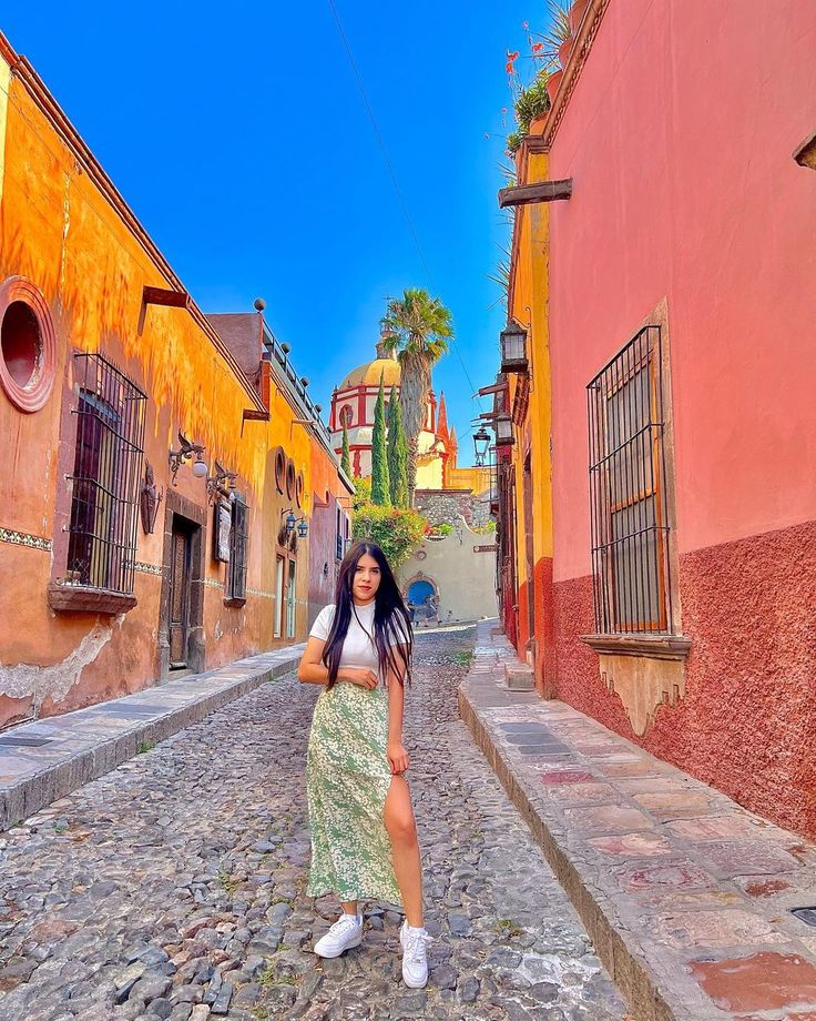 a woman standing in the middle of a cobblestone street with buildings on either side