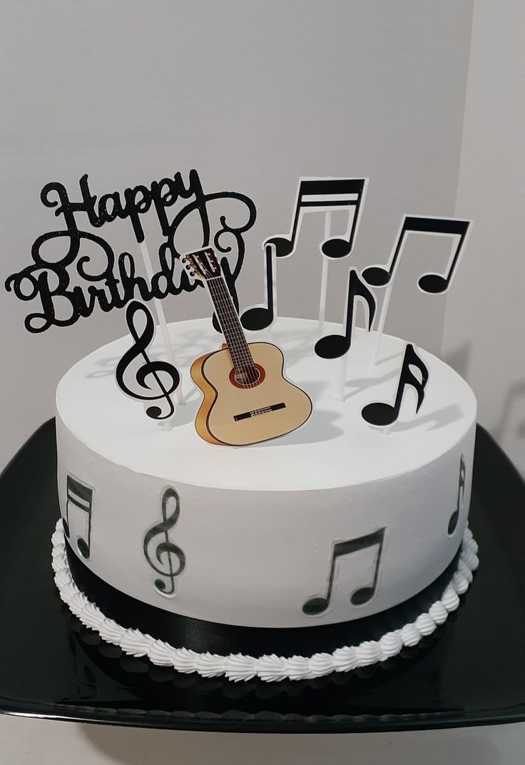 a birthday cake with musical notes and a guitar on it's top, sitting on a black platter