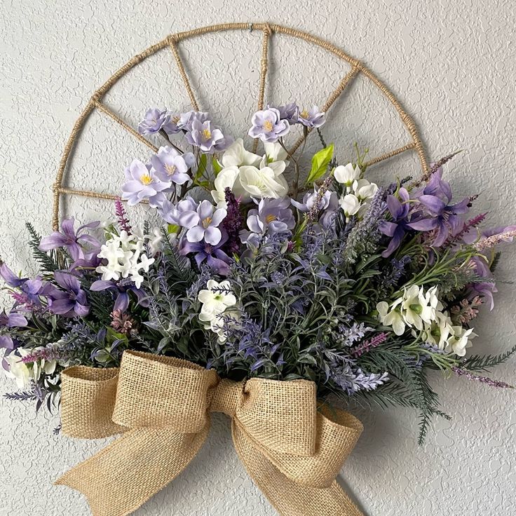 a bouquet of purple and white flowers hanging on a wall with a burlap bow