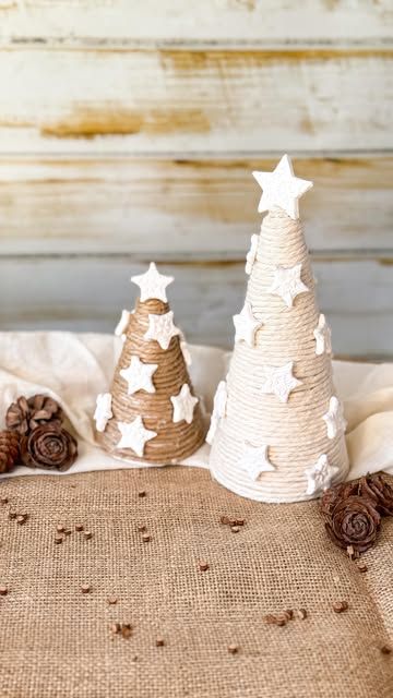 two small white christmas trees sitting on top of a burlock covered table cloth