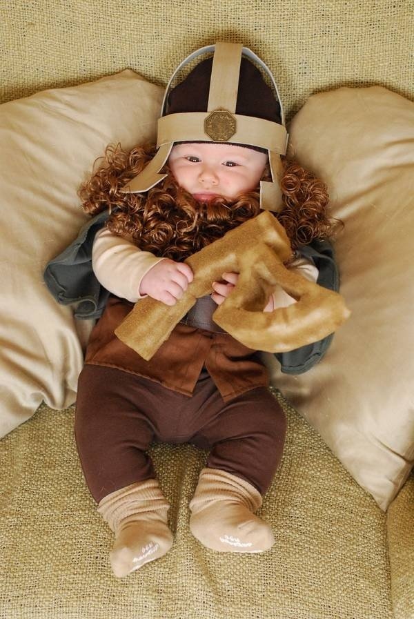 a baby wearing a helmet and holding a stuffed animal in it's lap while sitting on a couch