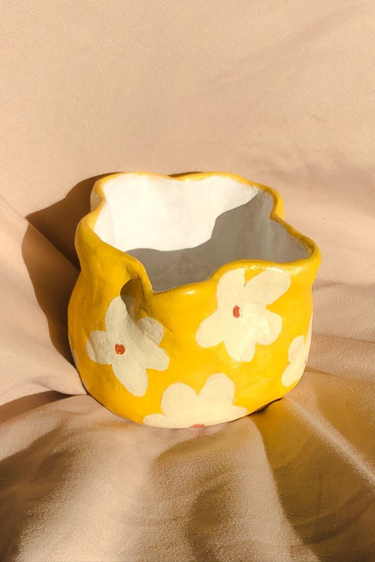 a yellow and white flower pot sitting on top of a bed next to a sheet