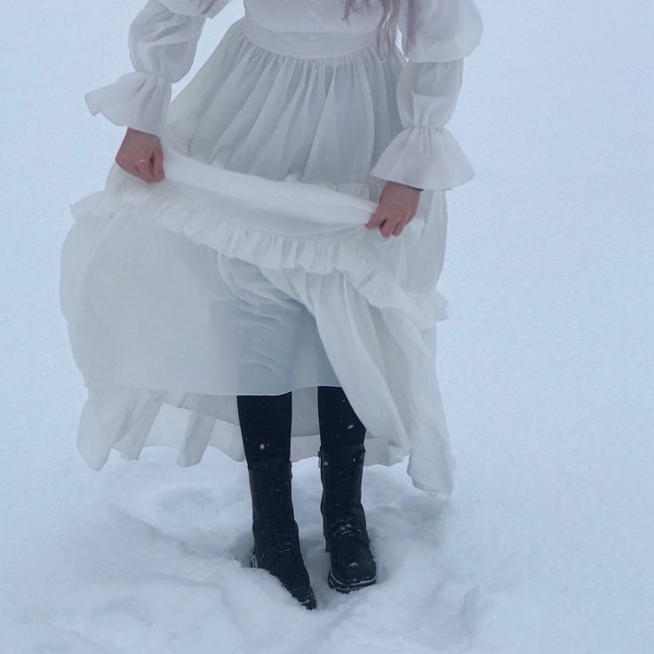 a woman standing in the snow wearing a white dress