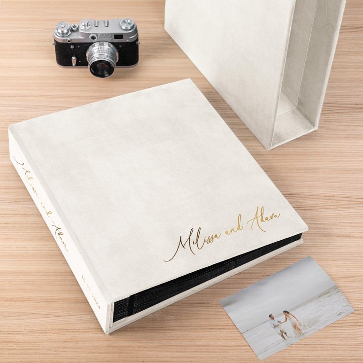 a wedding album with a camera next to it on a wooden table and an envelope