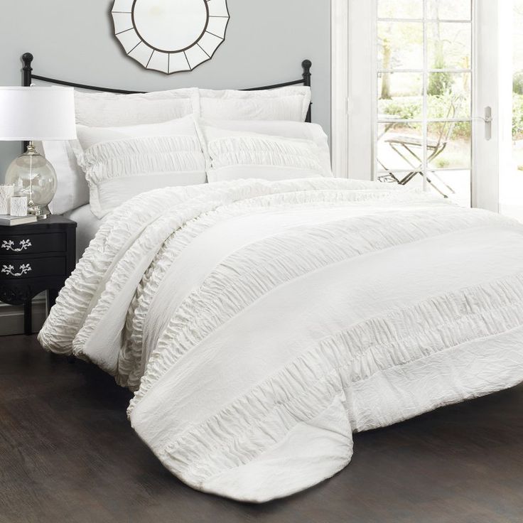 a bed with white comforter and pillows in a room next to a clock on the wall