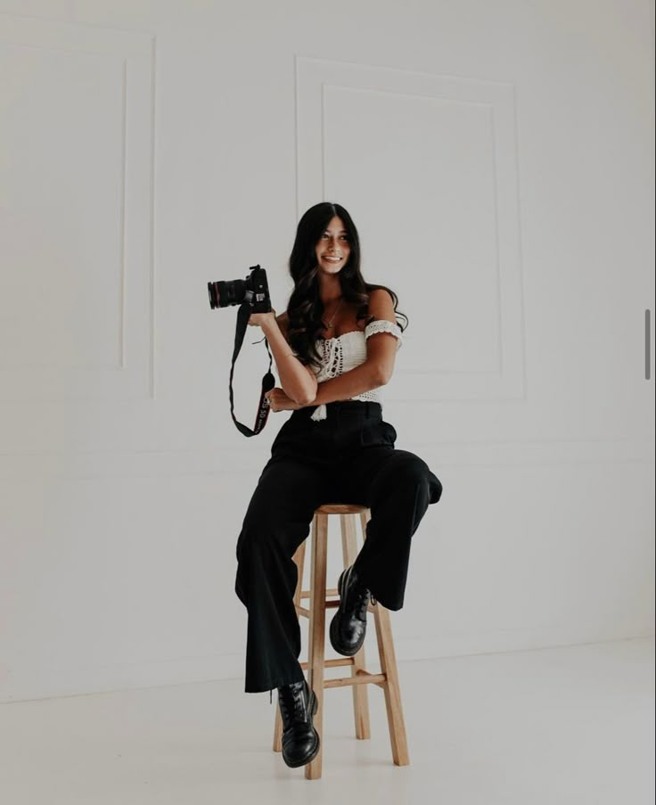 a woman sitting on top of a stool holding a camera