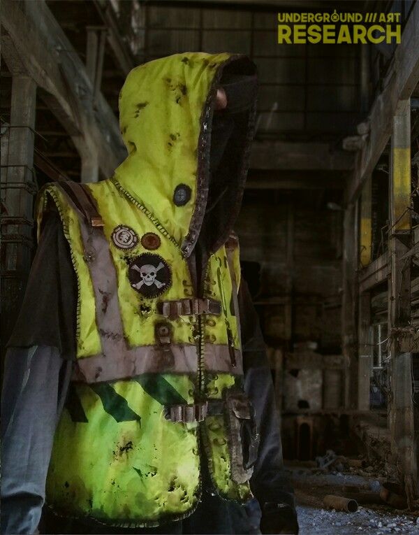 a man wearing a yellow vest and black jacket with a skull on the chest is standing in an abandoned building