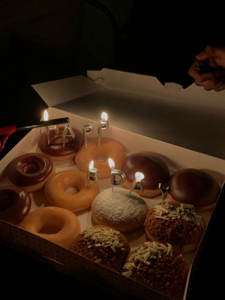 a box filled with lots of donuts sitting on top of a table next to candles