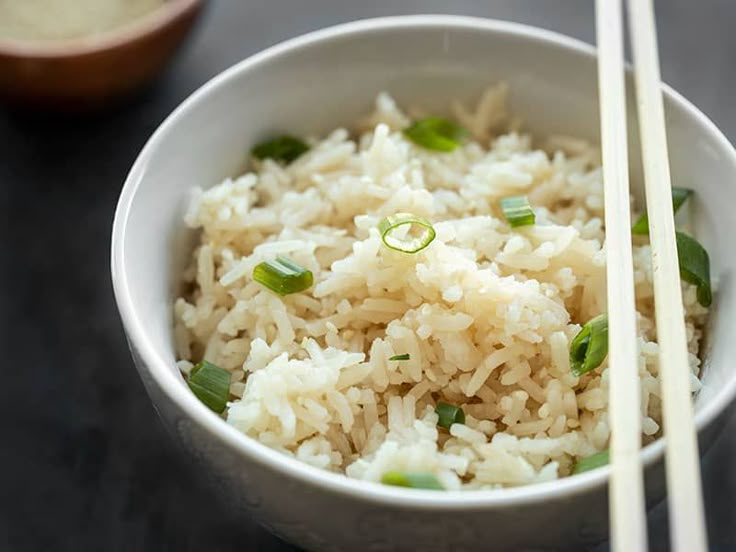 a white bowl filled with rice and chopsticks on top of a black table