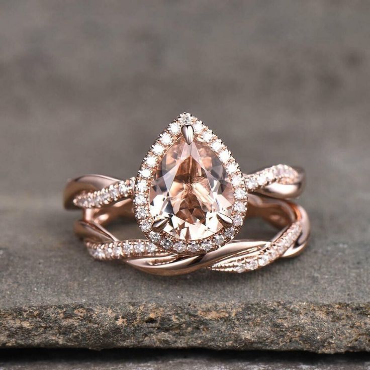 an engagement ring set with a pear shaped morganite surrounded by diamonds on top of a stone slab