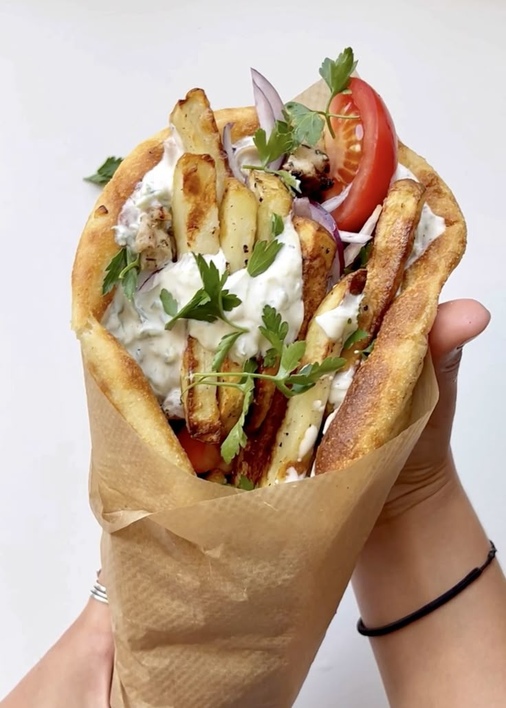 a person holding up a pita sandwich with vegetables and dressing on it's wrapper