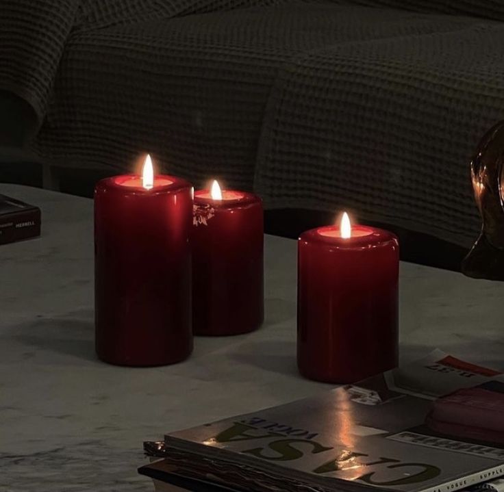 three red candles sitting on top of a table next to a magazine and a vase