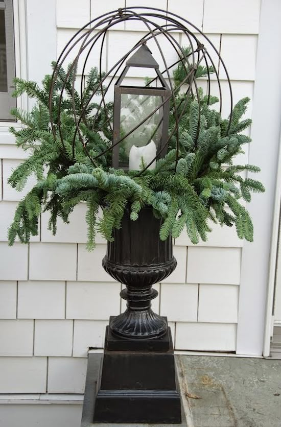 a planter filled with pine cones and evergreens in front of a white house