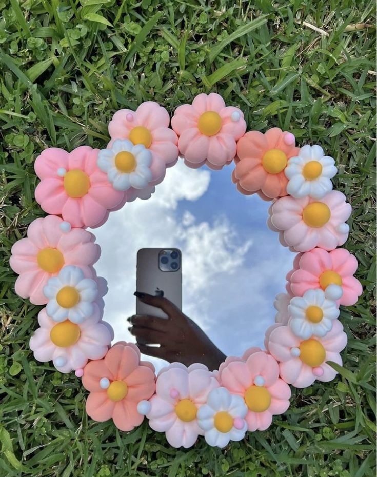 a hand holding a cell phone in front of a mirror with fake flowers on it