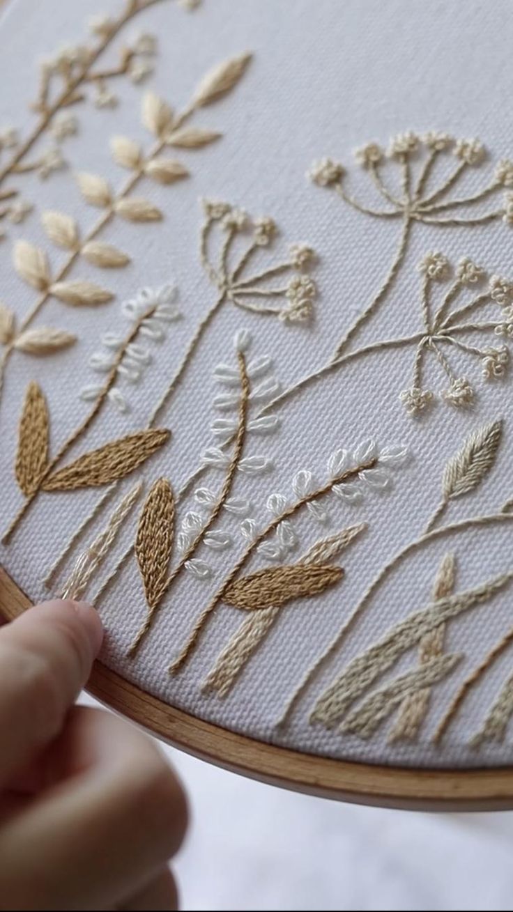 someone is stitching flowers on a white piece of fabric with gold thread and scissors