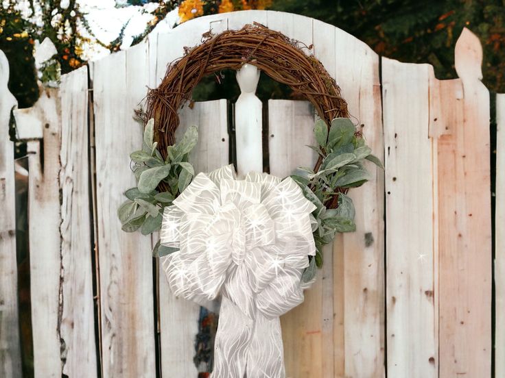 a white wreath hanging on the side of a wooden fence next to a picket fence