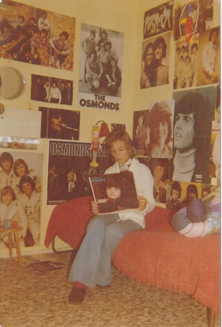 a person sitting on a bed reading a book in a room full of pictures and posters