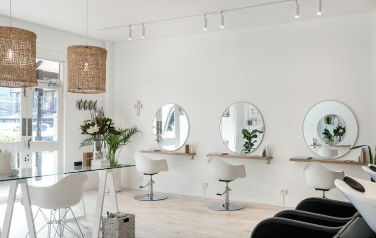 a salon with white chairs and mirrors on the wall, plants in vases next to them