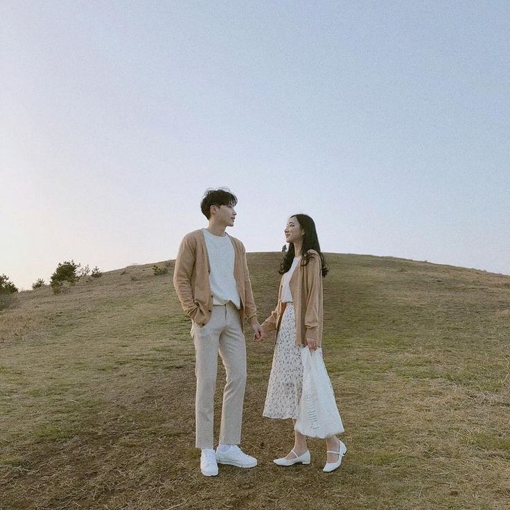 a man and woman standing on top of a grass covered hill next to each other