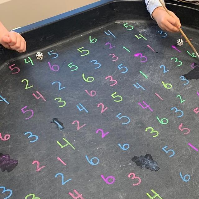 two children are playing with letters and numbers on a black tray that is filled with colored crayons