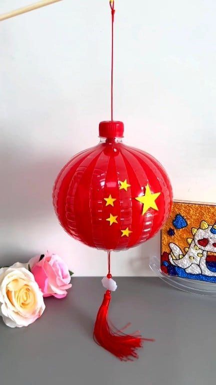 a red paper lantern with yellow stars on it next to a white rose and a cake