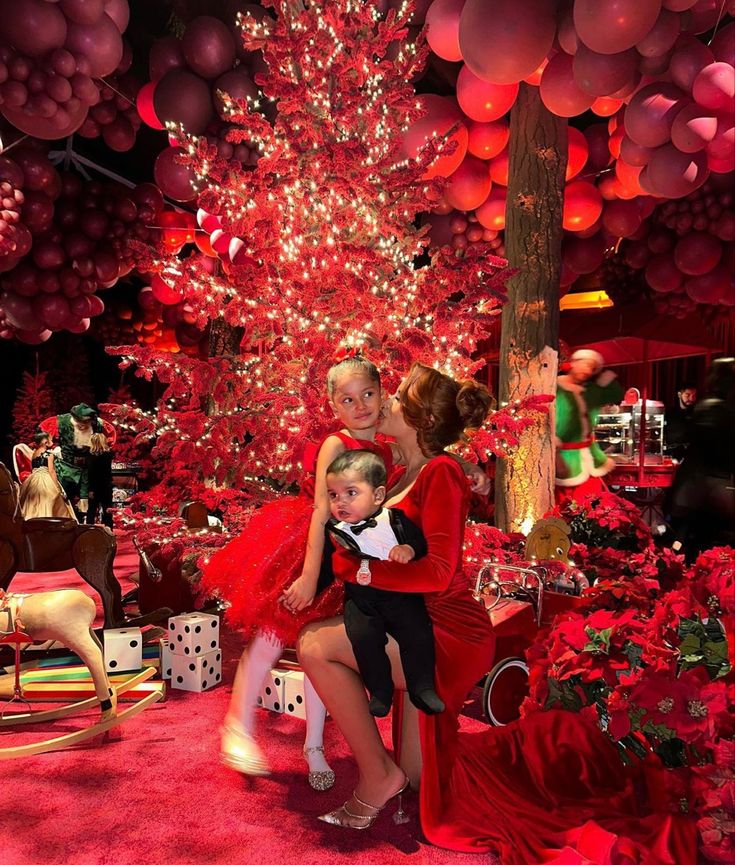 two women and a child are posing in front of a christmas tree with red decorations