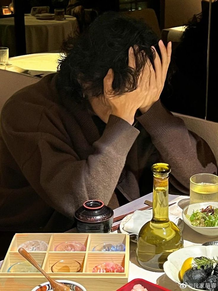 a man sitting at a table with food and drinks in front of him, covering his face