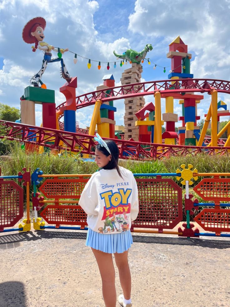 a woman standing in front of a toy story land roller coaster at the amusement park