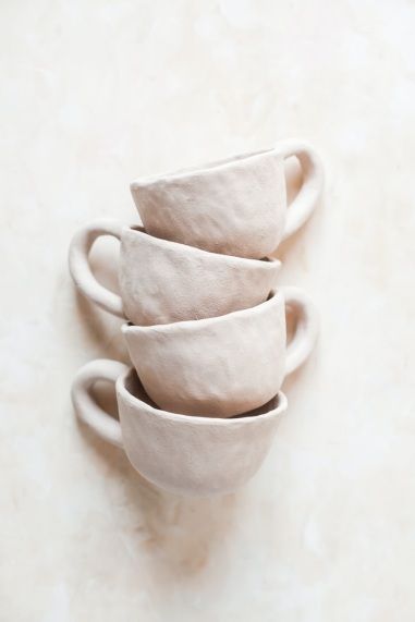 four white cups stacked on top of each other in a row against a beige wall