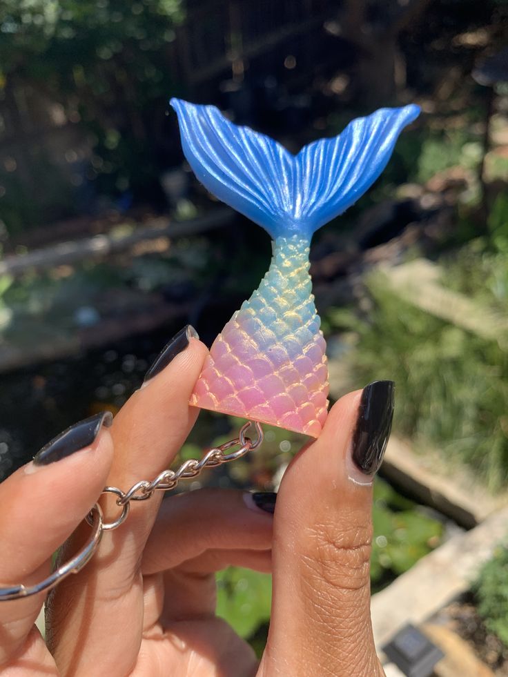 a hand holding a tiny blue and pink mermaid tail keychain in the shape of a fish