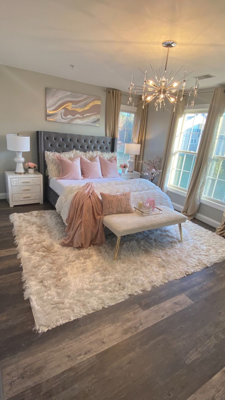 a bedroom with a large bed, chandelier and two windows in the room