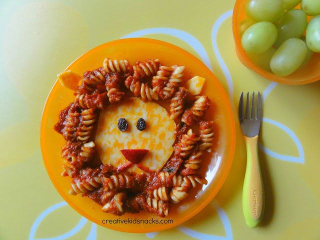 a yellow plate topped with pasta and a lion face on top of it next to grapes