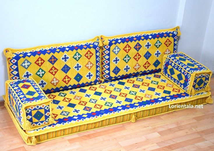 a yellow couch with blue and red designs on it's back cover sitting on a hard wood floor next to a white wall