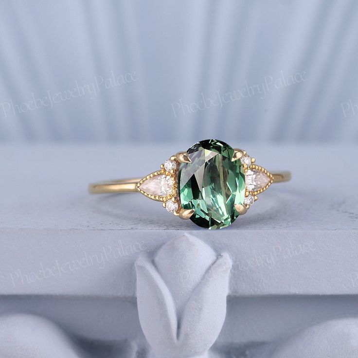 an oval green and white diamond ring on top of a white cloth covered tablecloth